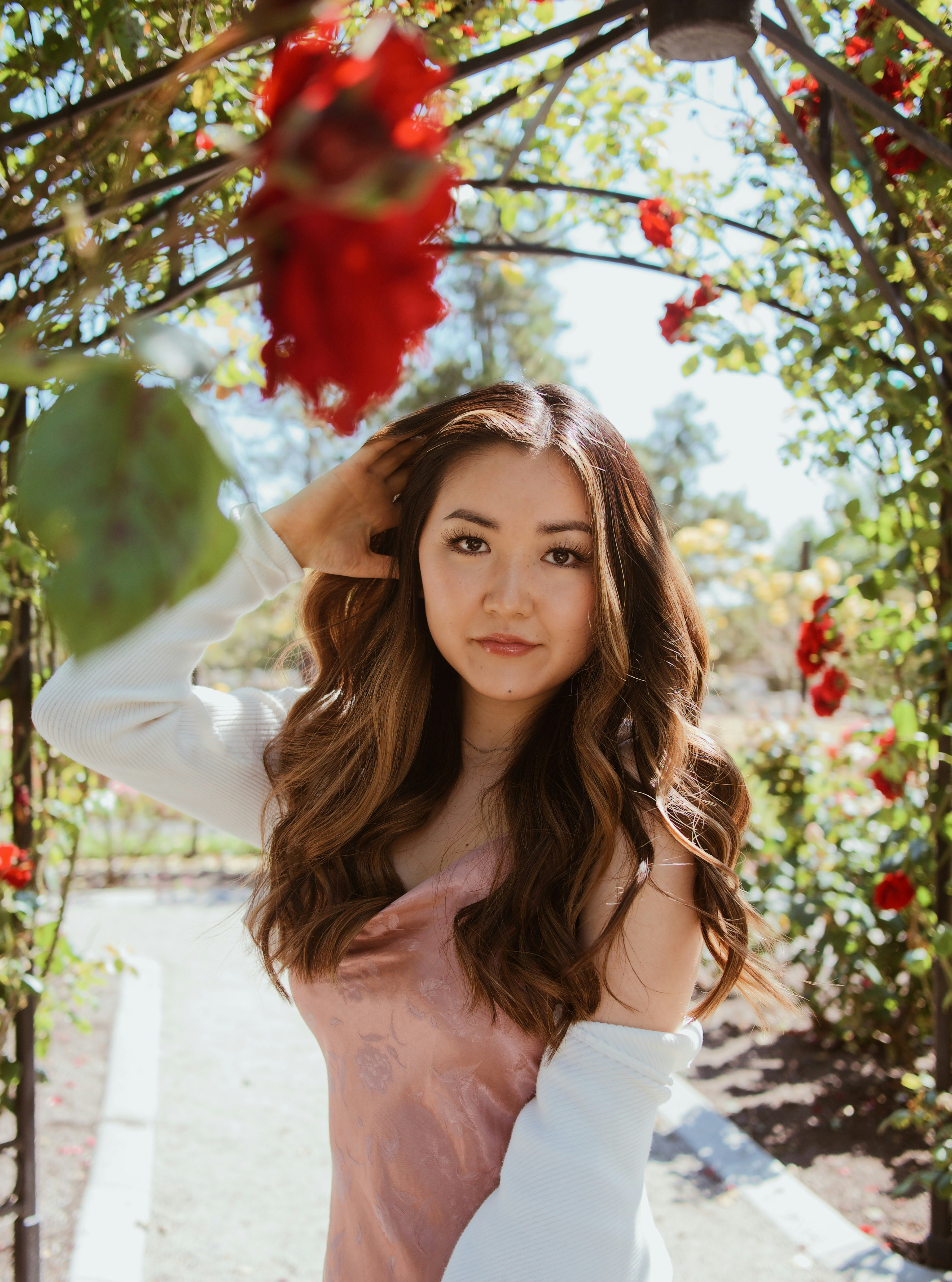 woman in white off shoulder shirt standing under red flowers