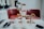 A sophisticated afternoon tea setting with a tiered tray filled with various pastries and desserts is arranged on a marble table. Two white teapots, cups, and saucers accompany the setup, alongside small dishes of condiments. Two red leather chairs are positioned in the background, adding a touch of elegance to the scene. The lighting is soft and natural, giving the space a welcoming ambiance.