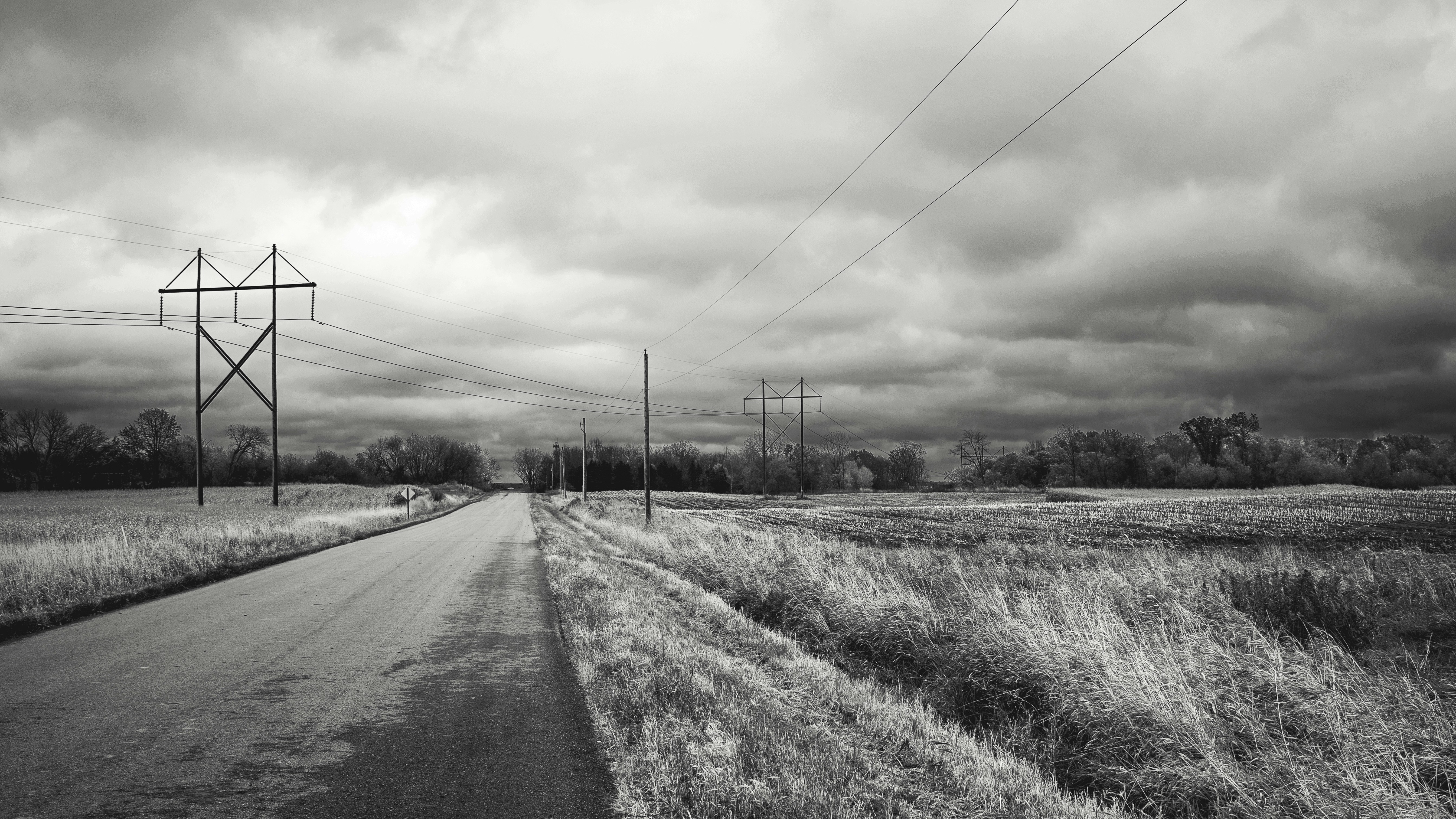 gray road between green grass field under white cloudy sky during daytime