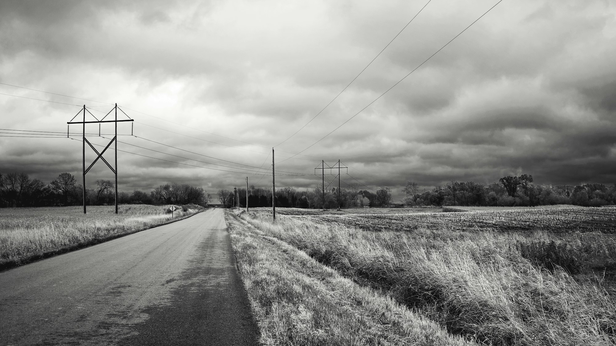 gray road between green grass field under white cloudy sky during daytime