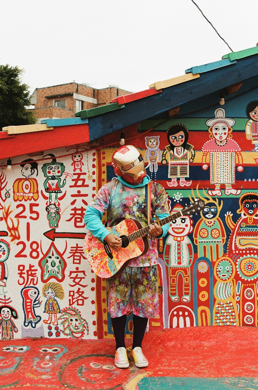 파란색과 흰색 스트라이프 긴 소매 셔츠를 입은 남자가 빨간색과 흰색 벽 근처에서 기타를 연주하고 있다