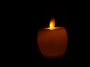 Close-up of a sleek black candle with a soft glowing flame on a minimalist white background