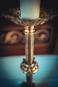 Close-up of hands polishing a weathered brass candlestick, set atop a dark wooden table with Victorian-era tools.
