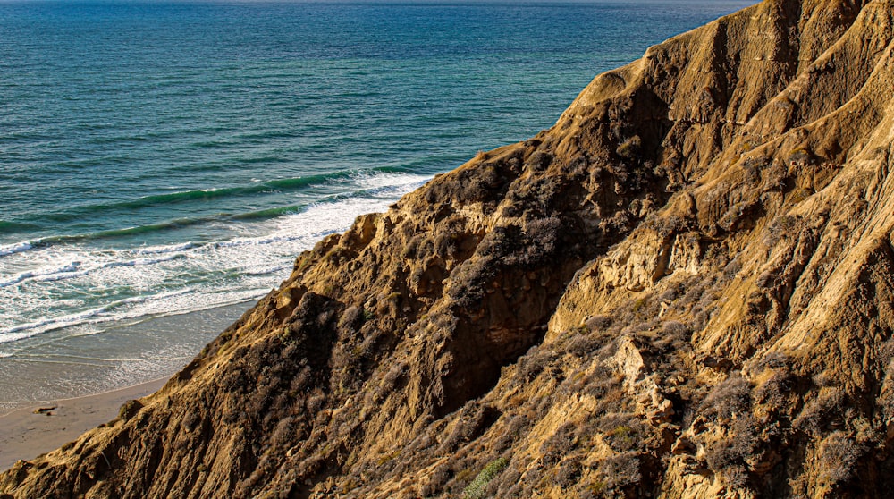 brown rocky mountain beside blue sea during daytime