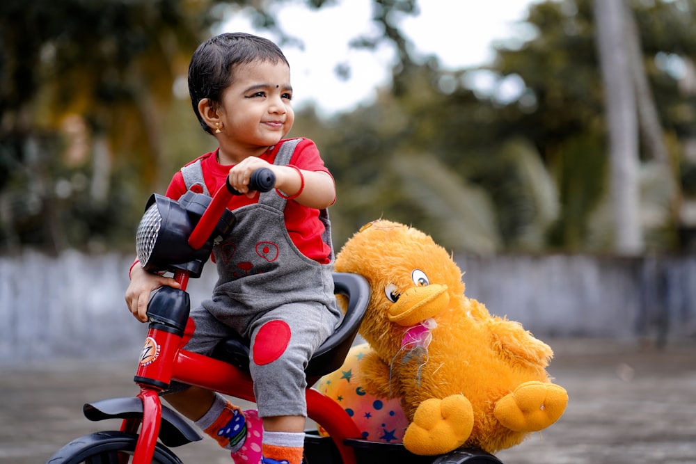 boy in blue denim jacket riding on bicycle with yellow bear plush toy during daytime