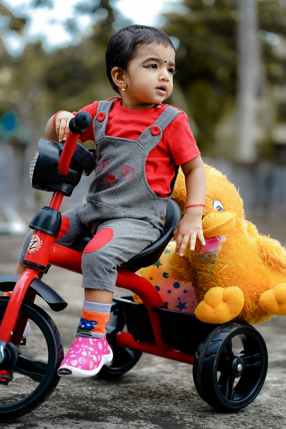 child in blue and red onesie riding on red bicycle