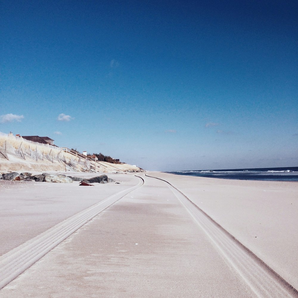 gray road between snow covered ground under blue sky during daytime