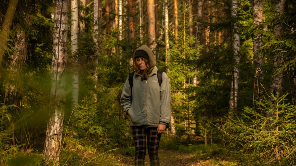 man in gray hoodie standing in the middle of forest during daytime