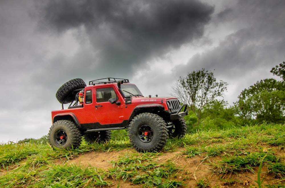 red and black jeep wrangler on green grass field under white clouds during daytime