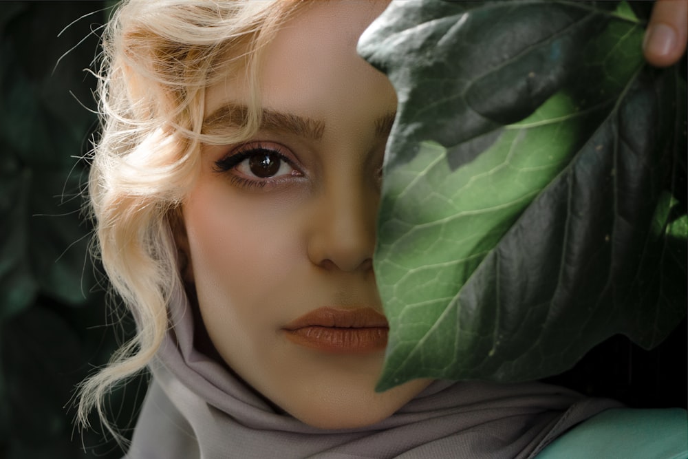 白いヒジャーブの女の子が緑の葉で顔を覆う