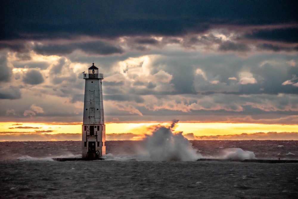 white and black lighthouse on sea under white clouds during daytime