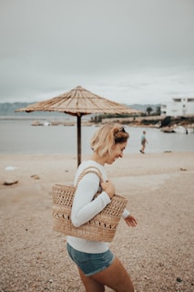 A cheerful young woman carrying a bright handmade bag along a sunny shoreline