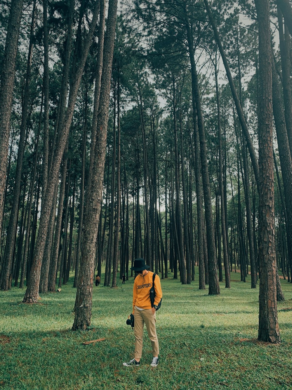 man in brown jacket walking on green grass field surrounded by trees during daytime