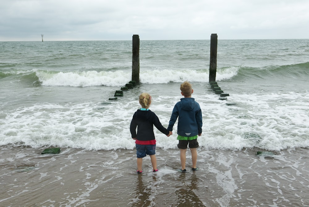 2 boys standing on beach during daytime