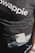 A person wearing a dark t-shirt with the word 'swappie' printed, partially tucked into blue denim jeans. A smartphone with multiple camera lenses is tucked into the pocket. The lower aspect of an arm and wrist with a woven bracelet is also visible.