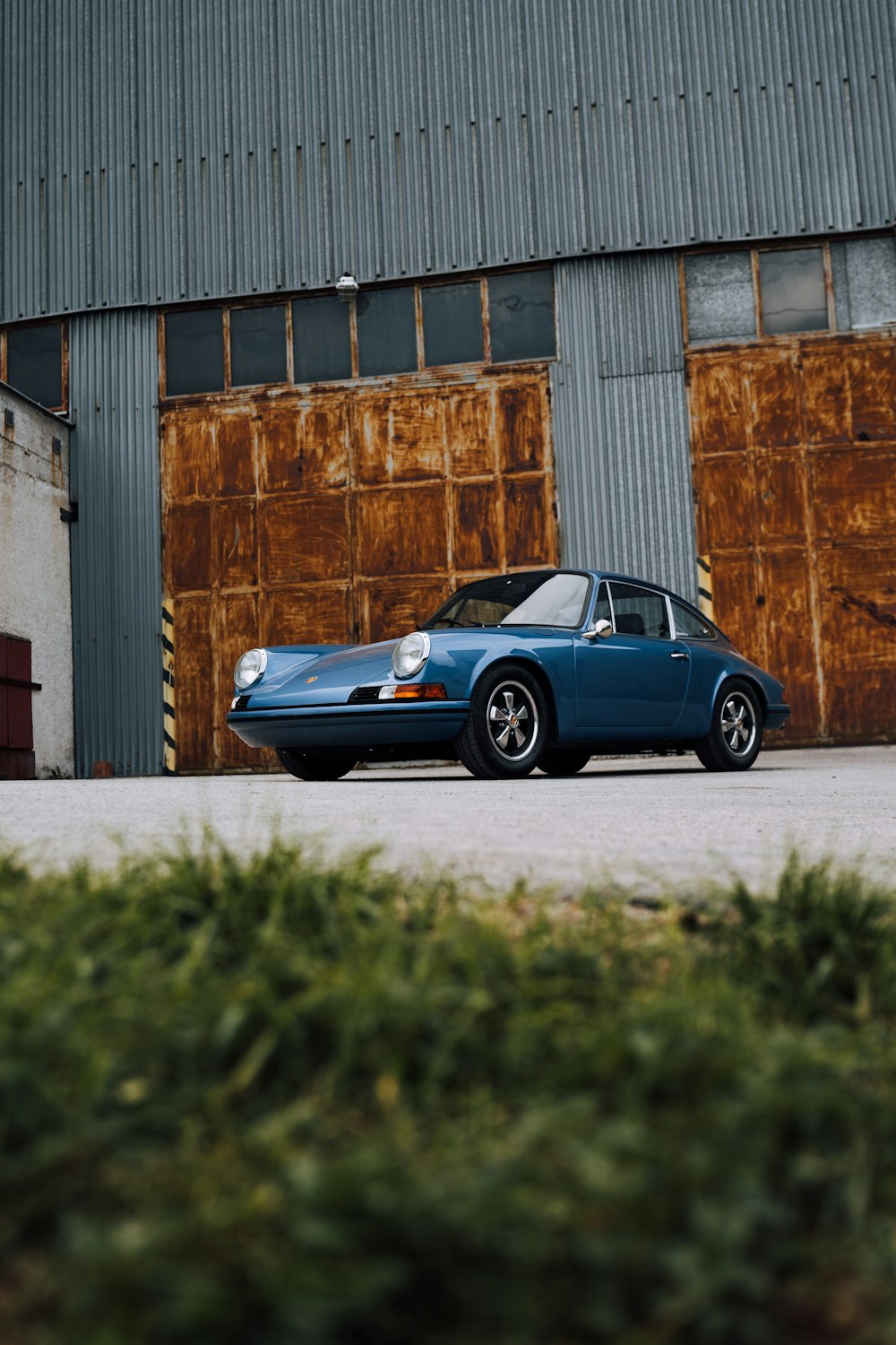 blue porsche 911 parked beside brown brick wall