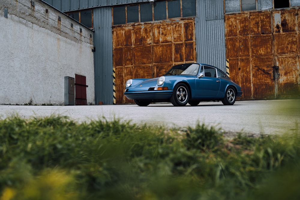 blue porsche 911 parked beside brown concrete building during daytime