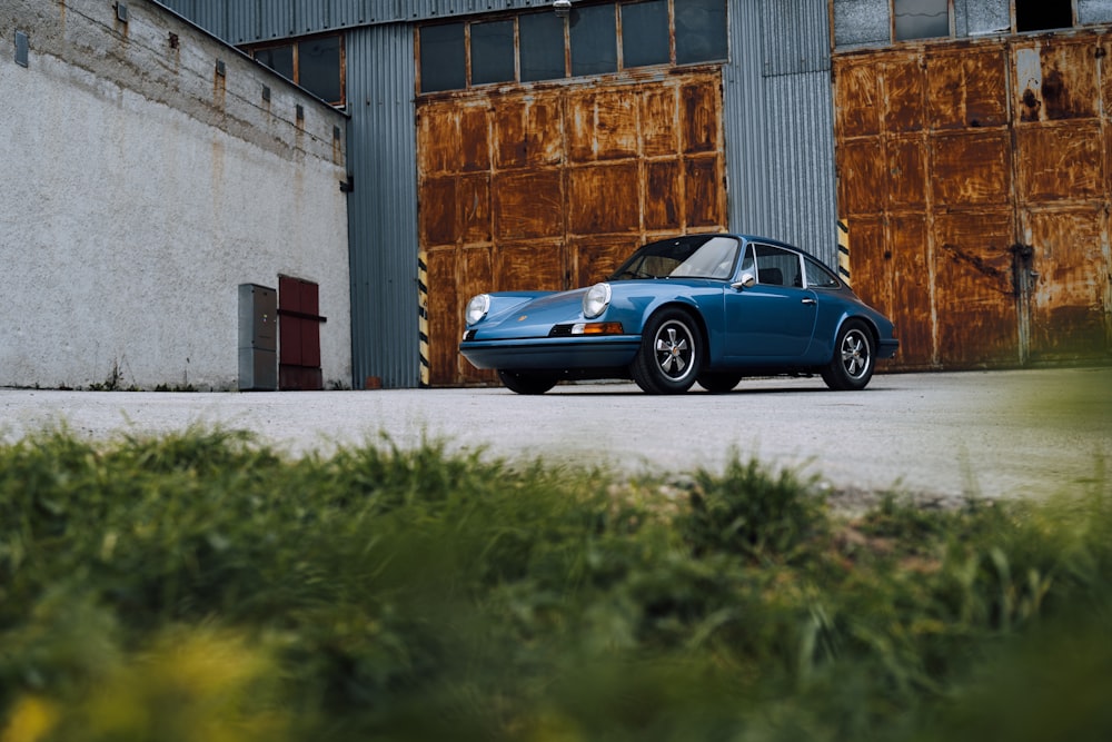 Porsche 911 azul estacionado junto a un edificio de hormigón marrón durante el día