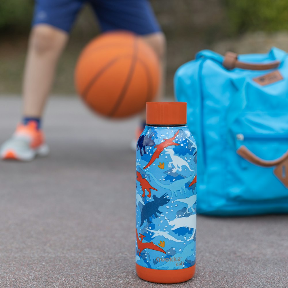 garrafa de plástico azul e branca ao lado da bola de basquete laranja no chão de concreto cinza durante o dia