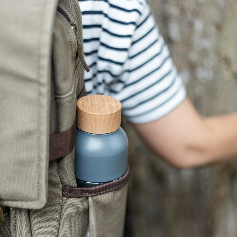 person in white and black striped shirt and brown pants holding blue and white plastic bottle