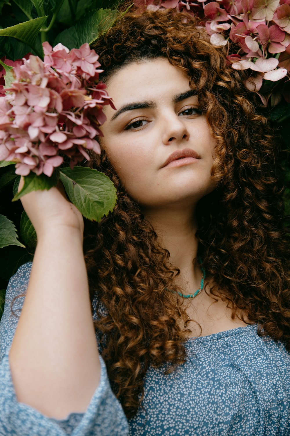 woman in blue sleeveless top holding pink flower