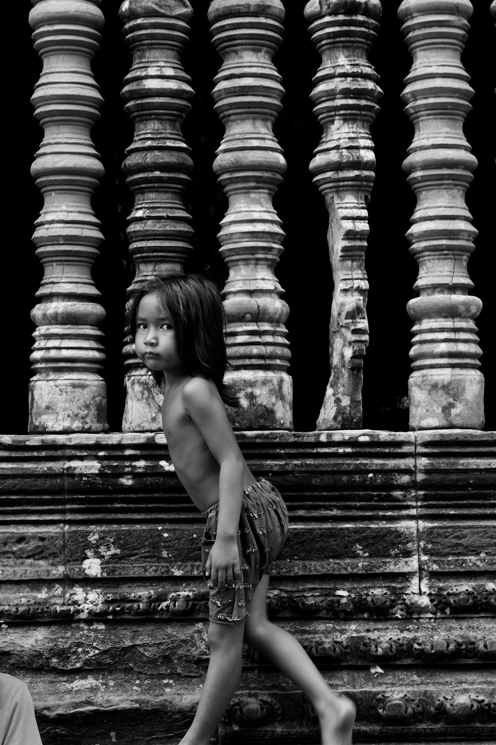 grayscale photo of topless woman sitting on concrete blocks