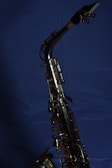 A brass saxophone with intricate keys and levers is set against a deep blue background. The polished metal surface reflects light, highlighting the instrument's craftsmanship.