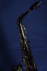 A brass saxophone with intricate keys and levers is set against a deep blue background. The polished metal surface reflects light, highlighting the instrument's craftsmanship.