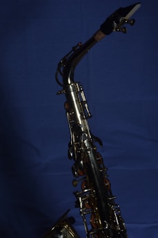 A brass saxophone with intricate keys and levers is set against a deep blue background. The polished metal surface reflects light, highlighting the instrument's craftsmanship.