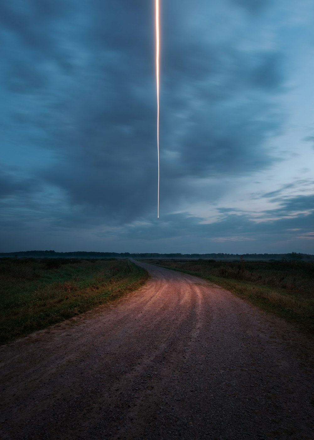 Graue Straße zwischen grünem Grasfeld unter grauen Wolken