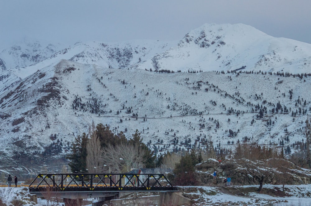brown wooden bridge over snow covered mountain