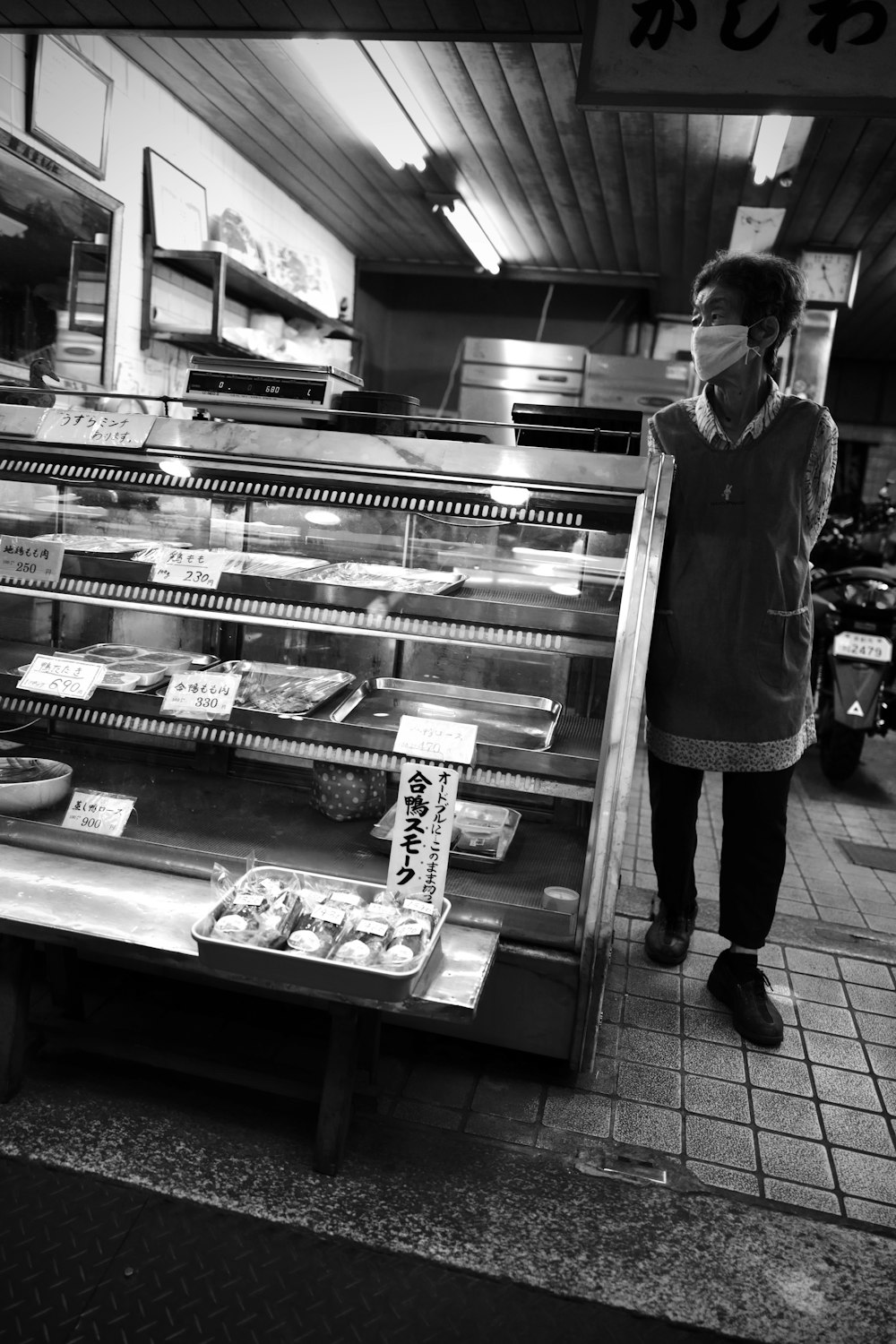 grayscale photo of woman in black jacket and black pants standing in front of display counter