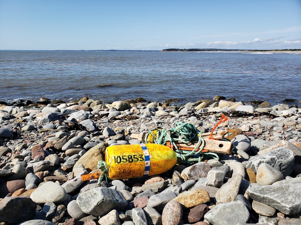 a yellow buoy laying on top of a rocky beach