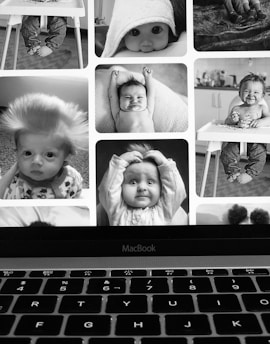 A collage of black and white baby photographs displayed on a laptop screen. The babies are captured in various poses and expressions, some smiling, others with surprised looks, and one with messy hair. The collage is visible above the keyboard of a MacBook.