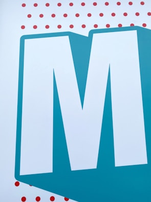 A large, bold, white letter 'M' is centered against a teal blue background. The letter is outlined with a thicker shade of teal that matches the background. Above and below the letter are multiple small, evenly spaced red dots on a white background.