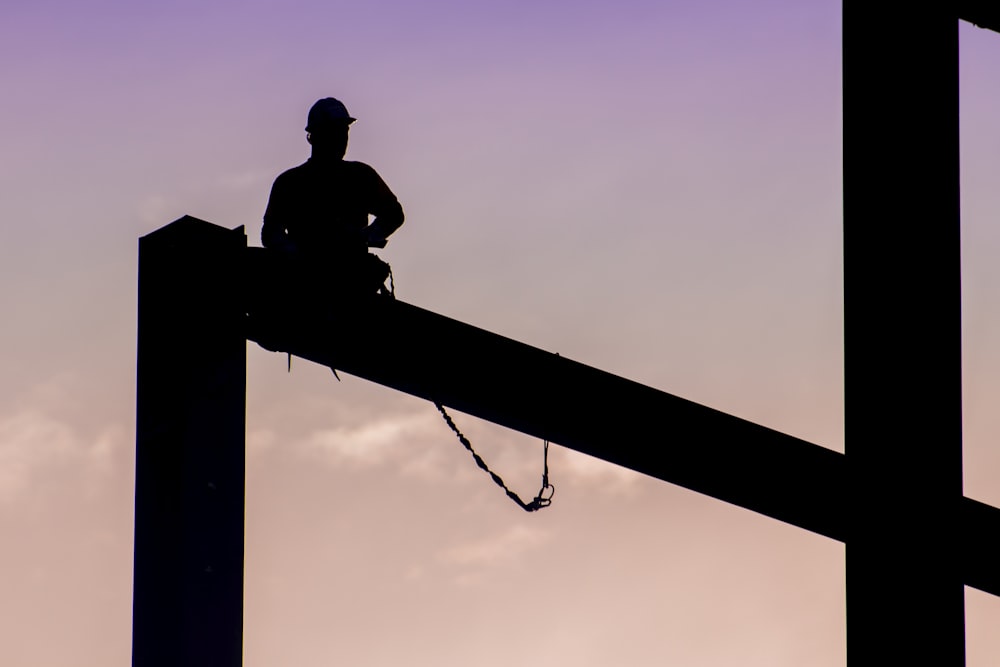 Silhouette d’un homme assis sur un poteau électrique pendant la journée