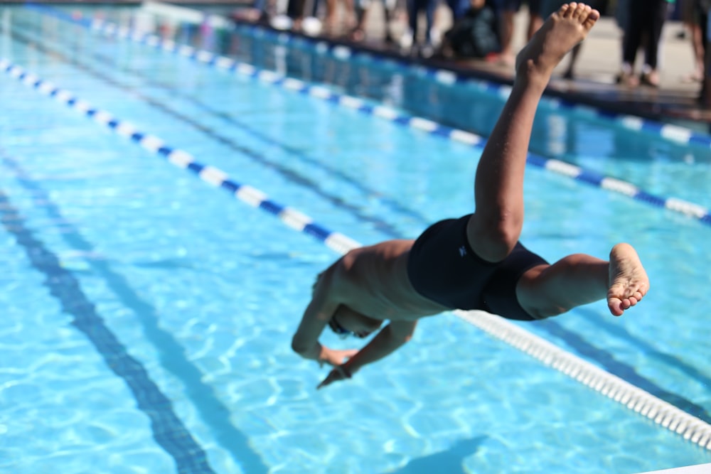 Frau in schwarzem Badeanzug springt tagsüber auf das Schwimmbad