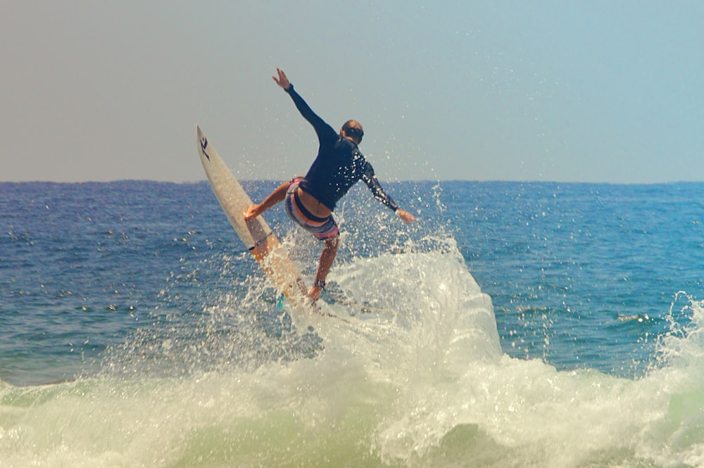 man in blue and black wet suit surfing on sea waves during daytime