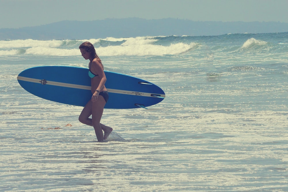 woman in blue bikini holding blue surfboard on beach during daytime