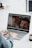 A person is using a laptop, which displays a video call with several smiling individuals on the screen. Their hands are on the keyboard, and there is a cup of coffee nearby.