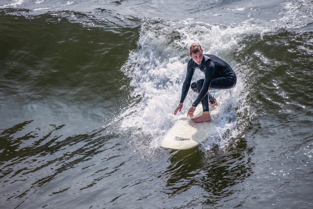 man in black wet suit riding white surfboard on water during daytime