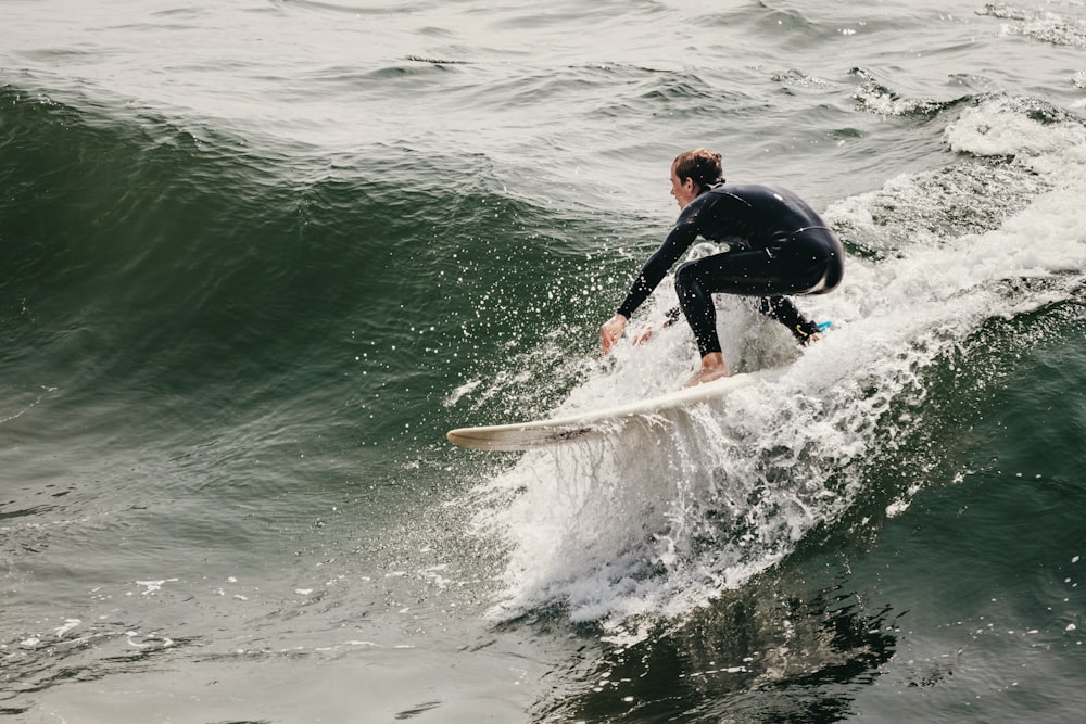 man in black wet suit riding white surfboard on green sea during daytime