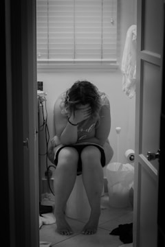 Close-up of a college girl sitting on a toilet with natural lighting.