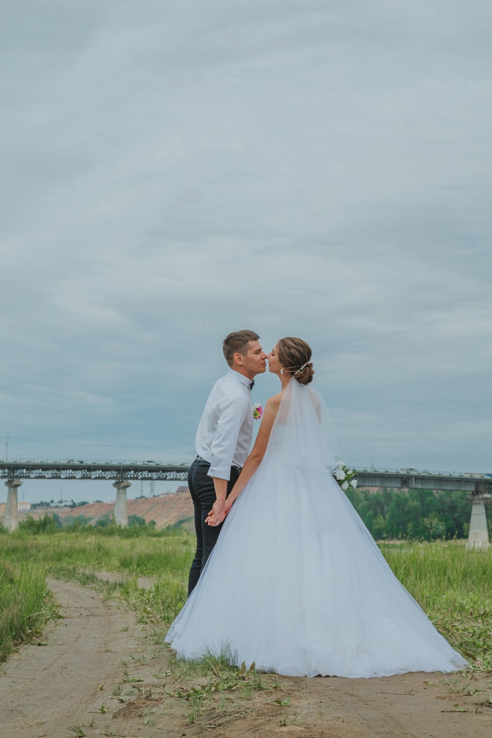 man in black suit and woman in white wedding dress standing on green grass field during