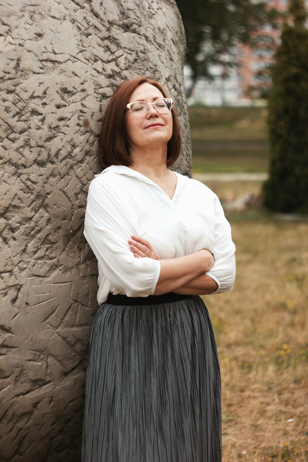 woman in white long sleeve shirt and black skirt standing beside brown tree during daytime