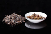 white ceramic bowl with brown dried leaves on black table