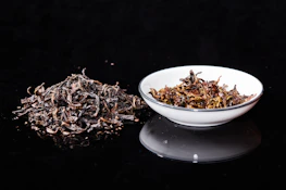 white ceramic bowl with brown dried leaves on black table