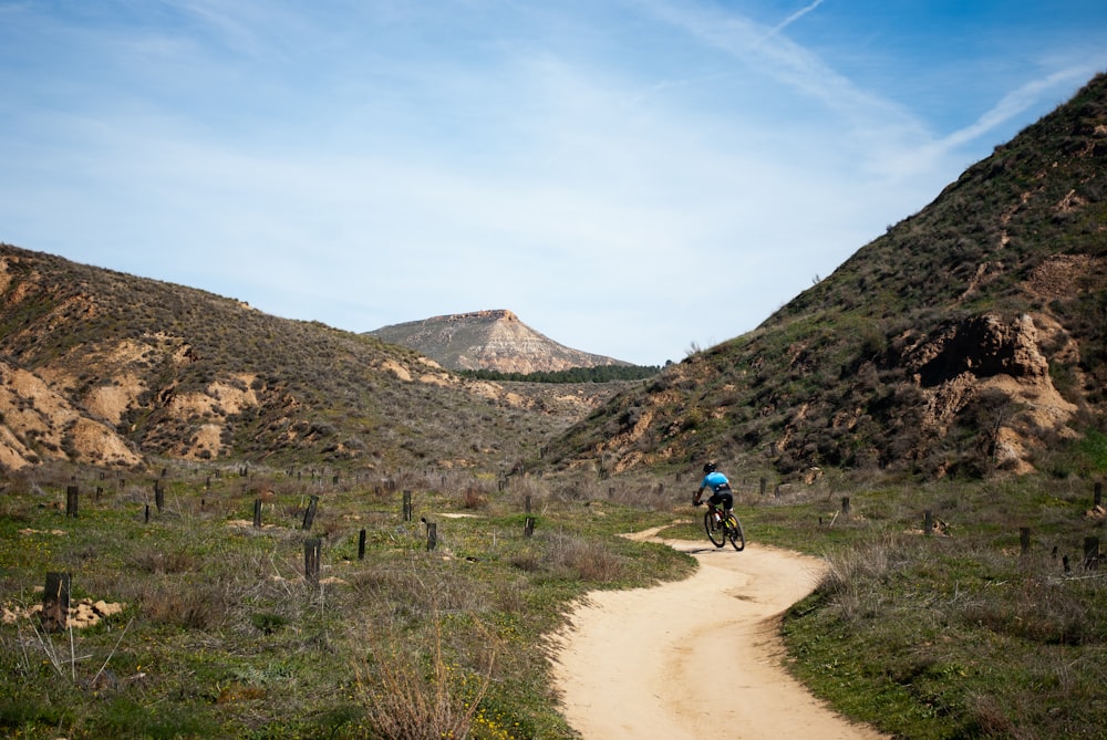 man riding motorcycle on dirt road near mountain during daytime