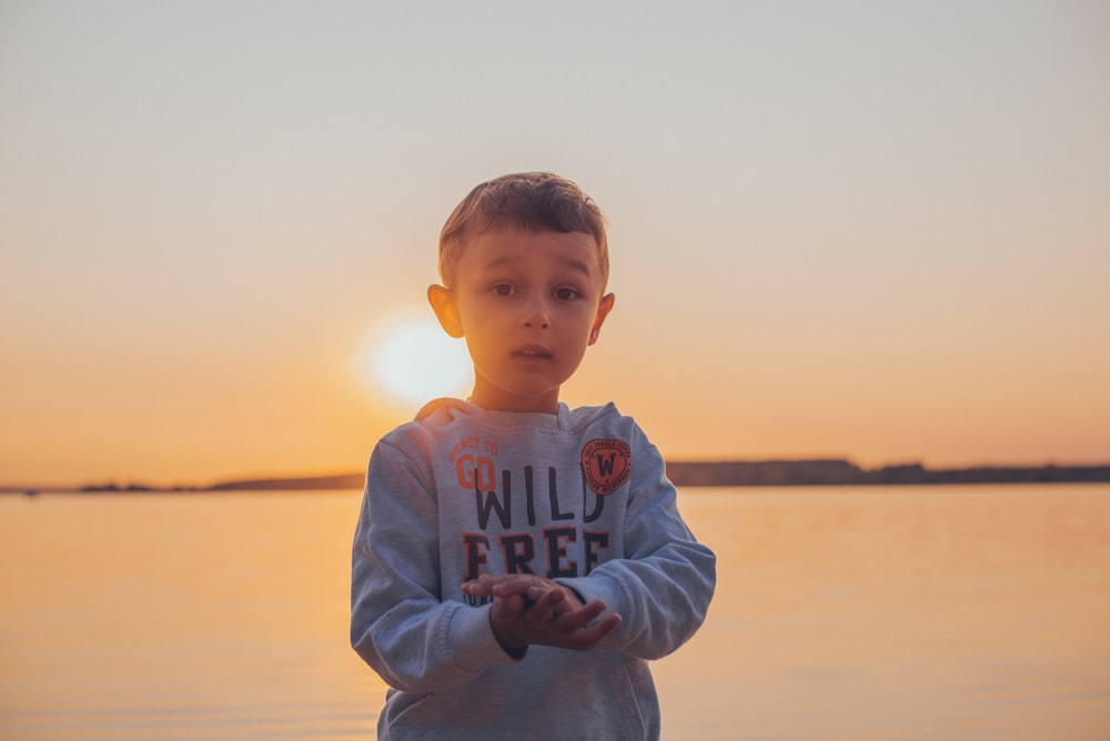 boy in white sweater standing on beach during sunset