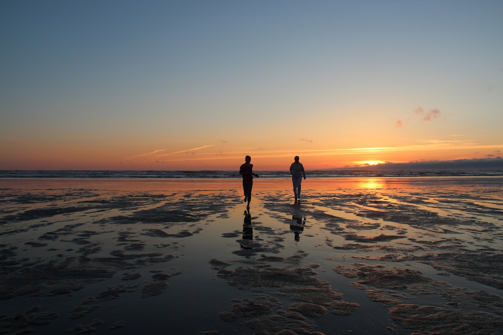 silhouette of man and woman standing on beach during sunset